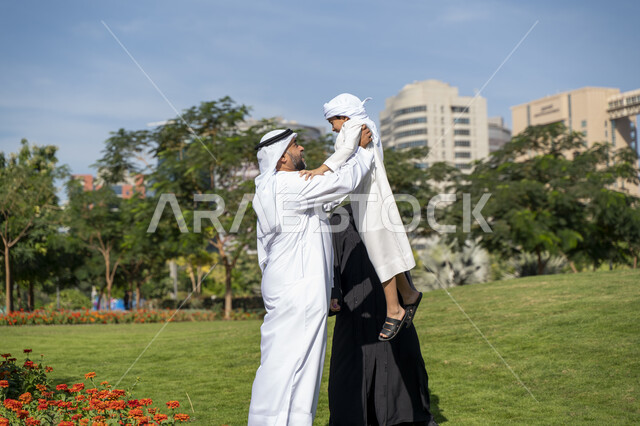 عائله عربيه إماراتية خليجيه مكونه من ثلاث أفراد, أب إماراتي يلعب مع ولده ويرفع به عاليا , قضاء وقت ممتع في الحديقه, رحله عائليه, مفهوم الأسره السعيده, إجازه صيفيه, الاستمتاع باللعب الجماعي في المنتزه, تسليه وترفيه