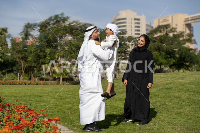 عائله عربيه إماراتية خليجيه مكونه من ثلاث أفراد, أب إماراتي يلعب مع ولده ويرفع به عاليا , قضاء وقت ممتع في الحديقه, رحله عائليه, مفهوم الأسره السعيده, إجازه صيفيه, الاستمتاع باللعب الجماعي في المنتزه, تسليه وترفيه