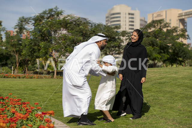 عائله عربيه إماراتية خليجيه مكونه من ثلاث أفراد, أب إماراتي يلعب مع ولده ويرفع به عاليا , قضاء وقت ممتع في الحديقه, رحله عائليه, مفهوم الأسره السعيده, إجازه صيفيه, الاستمتاع باللعب الجماعي في المنتزه, تسليه وترفيه