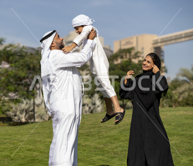 عائله عربيه إماراتية خليجيه مكونه من ثلاث أفراد, أب إماراتي يلعب مع ولده ويرفع به عاليا , قضاء وقت ممتع في الحديقه, رحله عائليه, مفهوم الأسره السعيده, إجازه صيفيه, الاستمتاع باللعب الجماعي في المنتزه, تسليه وترفيه