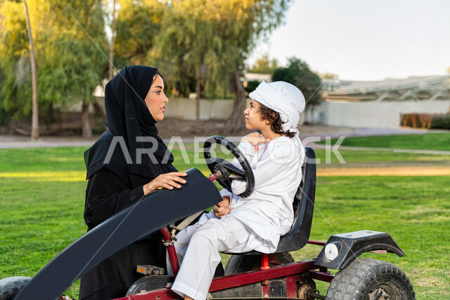 أم عربيه خليجية إماراتية ترتدي الزي التقلدي , إيماءات وجه تدل الحزن ,   اللعب بالدباب الكهربائي, مفهوم الأسرة السعيدة ، قضاء أوقات عائلية ممتعة, رحله عائليه في الصيف, اجازه صيفيه سعيده, عطلة نهاية الاسبوع, اللعب مع الابناء