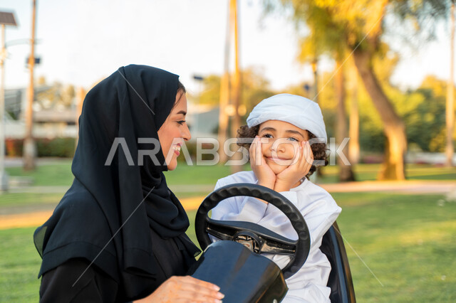 أم عربيه خليجية إماراتية ترتدي الزي التقلدي , إيماءات وجه تدل على الضحك و الكلام ,   اللعب بالدباب الكهربائي, مفهوم الأسرة السعيدة ، قضاء أوقات عائلية ممتعة, رحله عائليه في الصيف, اجازه صيفيه سعيده, عطلة نهاية الاسبوع, اللعب مع الابناء