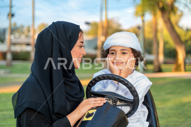 أم عربيه خليجية إماراتية ترتدي الزي التقلدي , إيماءات وجه تدل على الضحك و الكلام ,   اللعب بالدباب الكهربائي, مفهوم الأسرة السعيدة ، قضاء أوقات عائلية ممتعة, رحله عائليه في الصيف, اجازه صيفيه سعيده, عطلة نهاية الاسبوع, اللعب مع الابناء