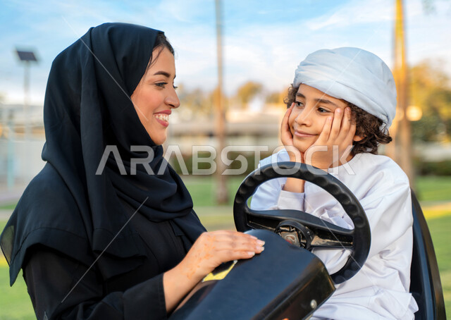 أم عربيه خليجية إماراتية ترتدي الزي التقلدي , إيماءات وجه تدل على الضحك و الكلام ,   اللعب بالدباب الكهربائي, مفهوم الأسرة السعيدة ، قضاء أوقات عائلية ممتعة, رحله عائليه في الصيف, اجازه صيفيه سعيده, عطلة نهاية الاسبوع, اللعب مع الابناء