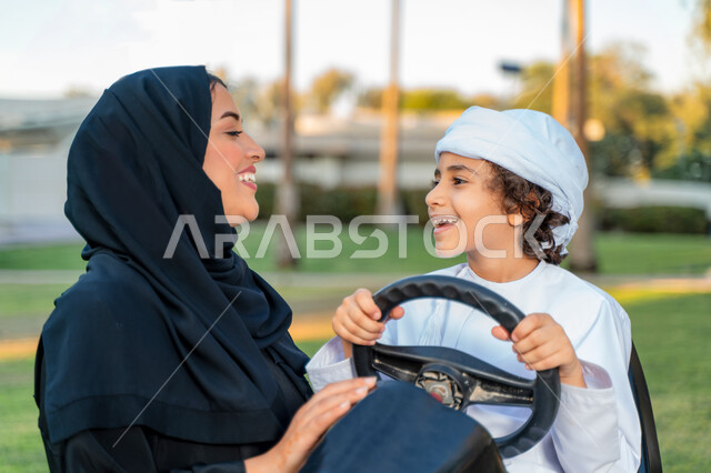 أم عربيه خليجية إماراتية ترتدي الزي التقلدي , إيماءات وجه تدل على الضحك و الكلام ,   اللعب بالدباب الكهربائي, مفهوم الأسرة السعيدة ، قضاء أوقات عائلية ممتعة, رحله عائليه في الصيف, اجازه صيفيه سعيده, عطلة نهاية الاسبوع, اللعب مع الابناء