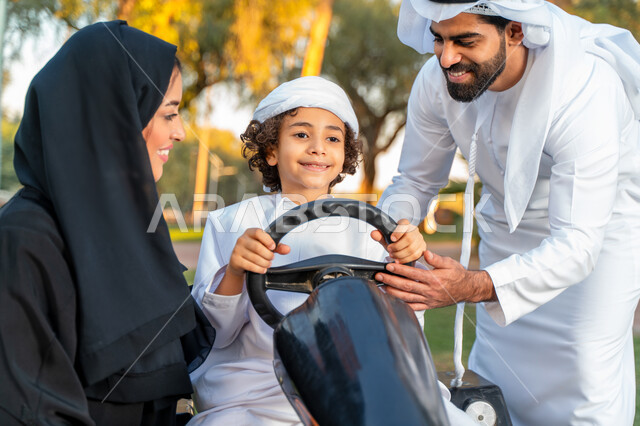 زوجان عربيان إماراتيان  خليجيان يلعبان مع ولدهم في الحديقه ، اللعب بالدباب الكهربائي, مفهوم الأسرة السعيدة ، قضاء أوقات عائلية ممتعة, رحله عائليه في الصيف, اجازه صيفيه سعيده, عطلة نهاية الاسبوع, اللعب مع الابناء
