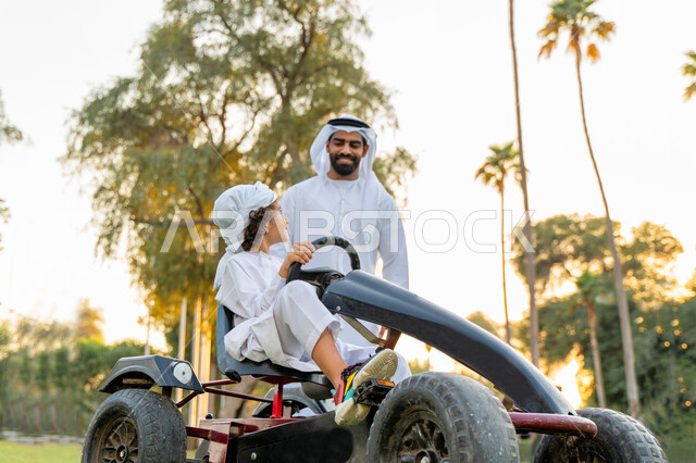 أب عربي خليجي إماراتي يرتدي الزي التقليدي يلعب مع ابنه في الحديقه ، اللعب بالدباب الكهربائي, مفهوم الأسرة السعيدة ، قضاء أوقات عائلية ممتعة, رحله عائليه في الصيف, اجازه صيفيه سعيده, عطلة نهاية الاسبوع, اللعب مع الابناء