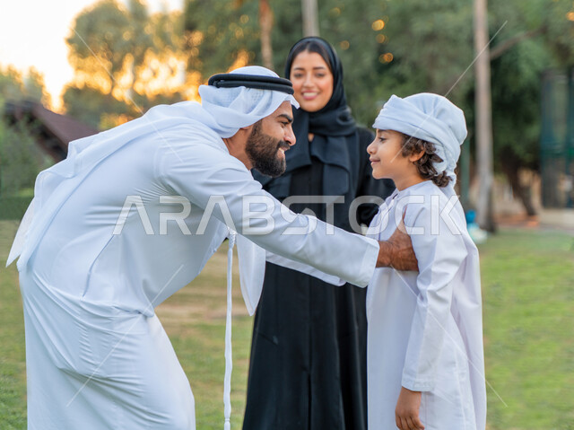 عائله عربيه إماراتيه  خليجيه مكونه من ثلاث أفراد, أب إماراتي يرتدي الزي التقليدي يلعب مع ابنه و يرفعه عاليا , رحله عائليه عند غروب الشمس , مفهوم الأسره السعيده, إجازه صيفيه, الاستمتاع باللعب الجماعي في المنتزه, تسليه وترفيه, عطلة نهاية الاسبوع