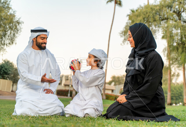 عائله عربيه إماراتيه  خليجيه مكونه من ثلاث أفراد, قضاء وقت ممتع في الحديقه عند غروب الشمس , اللعب الجماعي بالكره في المنتزه, تسليه وترفيه, عطلة نهاية الاسبوع