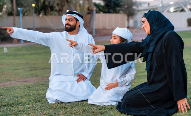 عائله عربيه إماراتيه  خليجيه مكونه من ثلاث أفراد, قضاء وقت ممتع في الحديقه, الإشارة الى شيء ما, رحله عائليه في يوم مشمس, مفهوم الأسره السعيده, إجازه صيفيه, الاستمتاع باللعب الجماعي في المنتزه, تسليه وترفيه, عطلة نهاية الاسبوع
