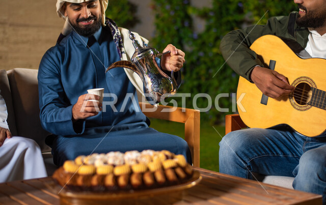 صورة مقربة لمجموعة من الشباب العرب الخليجيين السعوديين يقضون أوقات ممتعة في إحدى الشاليهات السياحية بالسعودية، شاب يعزف على آلة القيثارة واخر يقوم بصب القهوة، أجواء شتوية، أجواء شبابية سعيدة، جلسة وناسة وتعارف، إجتماع الأصدقاء، سهرة شبابية