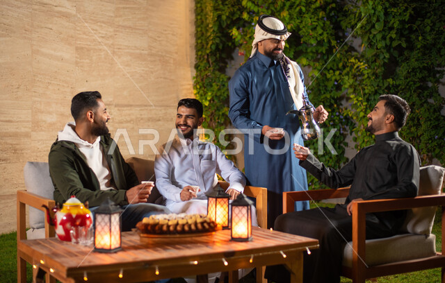 A close-up of a group of Saudi Gulf Arab youth spending fun times in one of the tourist chalets in Saudi Arabia, a young man pouring coffee, a winter atmosphere, a happy youth atmosphere, a session with people and acquaintance, a meeting of friends, a you