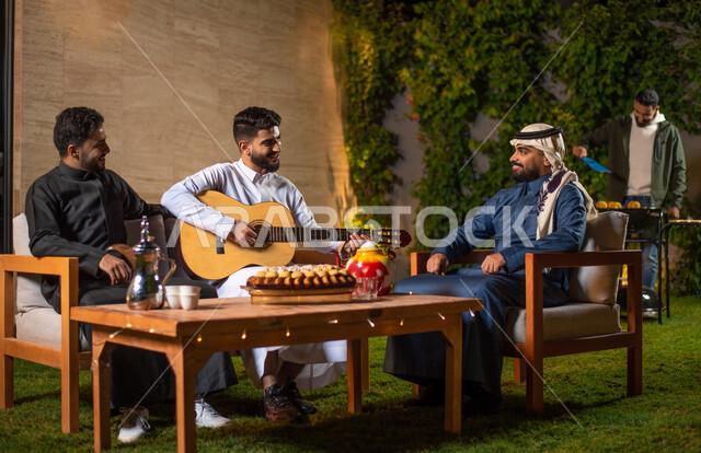مجموعة من الشباب العرب الخليجيين السعوديين يقضون أوقات ممتعة في إحدى الشاليهات السياحية بالسعودية، فعاليات شبابية ترفيهية، شاب يعزف على آلة القيثارة، أجواء شتوية، جلسة وناسة وتعارف، إجتماع الأصدقاء، سهرة شبابية