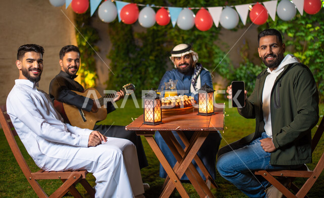 مجموعة من الشباب العرب الخليجيين السعوديين يقضون أوقات ممتعة في إحدى الشاليهات السياحية بالسعودية، هاتف محمول بشاشة سوداء فارغة، عرض خدمات وتطبيقات الهاتف المحمول، أجواء شتوية، جلسة وناسة وتعارف، إجتماع الأصدقاء، سهرة شبابية