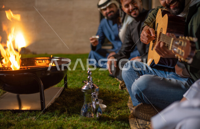 صورة مقربة لمجموعة من الشباب العرب الخليجيين السعوديين يقضون أوقات ممتعة في إحدى الشاليهات السياحية بالسعودية، فعاليات شبابية ترفيهية، شاب يعزف على آلة القيثارة، أجواء شتوية، أجواء شبابية سعيدة، جلسة وناسة وتعارف، إجتماع الأصدقاء، سهرة شبابية