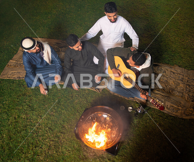 مجموعة من الشباب العرب الخليجيين السعوديين يقضون أوقات ممتعة في إحدى الشاليهات السياحية بالسعودية، فعاليات شبابية ترفيهية، شاب يعزف على آلة القيثارة، أجواء شتوية، أجواء شبابية سعيدة، قضاء أوقات ممتعة، جلسة وناسة وتعارف، إجتماع الأصدقاء، سهرة شبابية