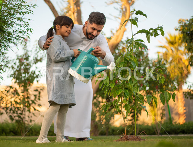 رجل عربي خليجي سعودي يقضي وقت ممتع مع إبنته في ري الأشجار بإستخدام وعاء السقي ، فعاليات وأجواء ترفيهية ، تعابير تدل على السعادة ، خلفية الطبيعة ، الأِشجار الطبيعية الخضراء ، التسليه والترفيه ، مشاركة عائلية