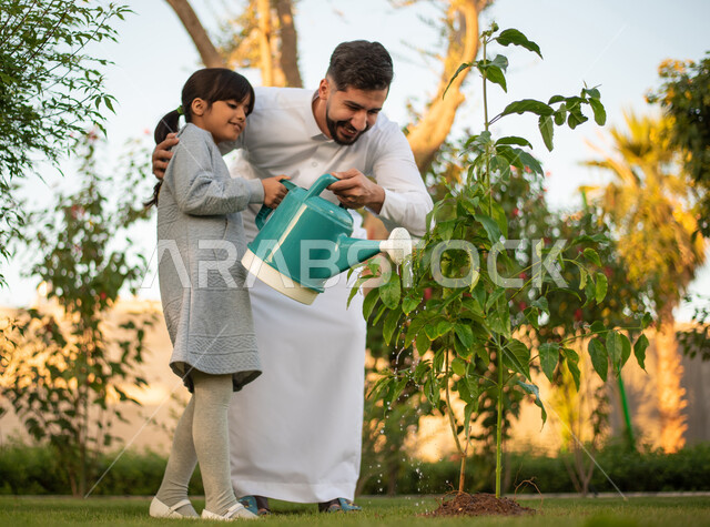رجل عربي خليجي سعودي يقضي وقت ممتع مع إبنته في ري الأشجار بإستخدام وعاء السقي ، فعاليات وأجواء ترفيهية ، تعابير تدل على السعادة ، خلفية الطبيعة ، الأِشجار الطبيعية الخضراء ، التسليه والترفيه ، مشاركة عائلية