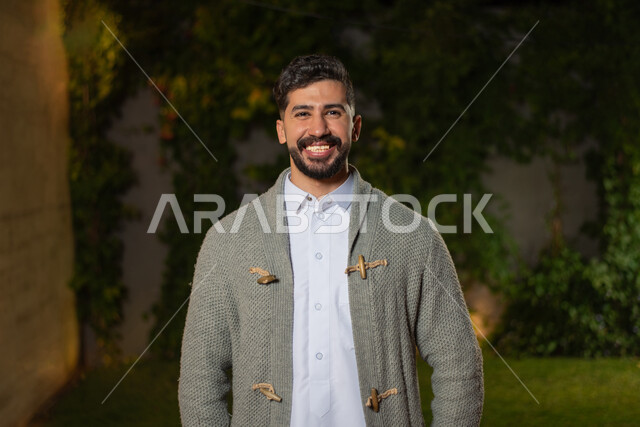 صورة مقربة لرجل عربي خليجي سعودي ، مبتسم ينظر إلى الكاميرا ، تعابير وجه تدل على السعادة ، أزياء الشتاء ، ملابس شتوية ، خلفية الطبيعة