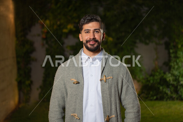 صورة مقربة لرجل عربي خليجي سعودي ، مبتسم ينظر إلى الكاميرا ، تعابير وجه تدل على السعادة ، أزياء الشتاء ، ملابس شتوية ، خلفية الطبيعة