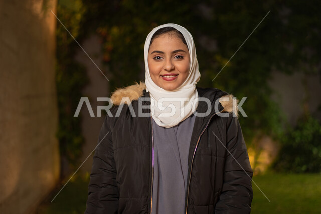 صورة مقربة لمرأة عربية خليجية سعودية ، مبتسمة تنظر إلى الكاميرا ، تعابير وجه تدل على السعادة ، أزياء الشتاء ، ملابس شتوية ، خلفية الطبيعة