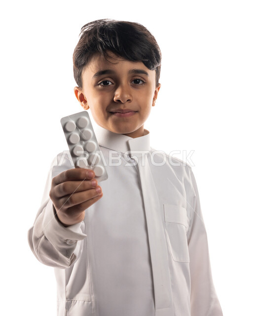بورتريه لولد عربي خليجي سعودي، ينظر إلى الكاميرا، يحمل بيده شريط الدواء ، إستخدام الدواء بوصفة طبية ، علاج الآلام والأوجاع ، مفهوم الصيدلة ، مستلزمات طبية ، أدوية وعقاقير طبية ، خلفية بيضاء