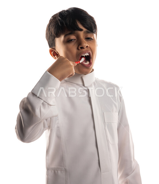 Portrait of a Saudi Arabian Gulf boy brushing his teeth with a toothbrush, the concept of care and concern for dental health and hygiene, daily oral hygiene routine, treatment of tooth decay for children, white background