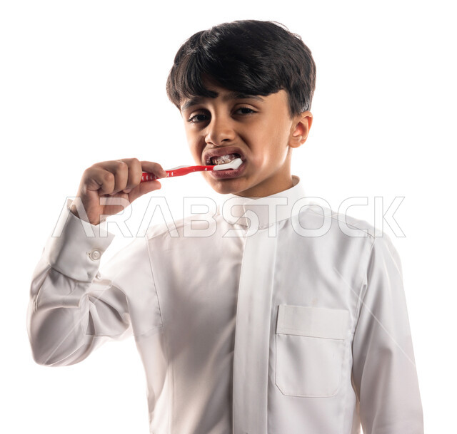 Portrait of a Saudi Arabian Gulf boy brushing his teeth with a toothbrush, the concept of care and concern for dental health and hygiene, daily oral hygiene routine, treatment of tooth decay for children, white background