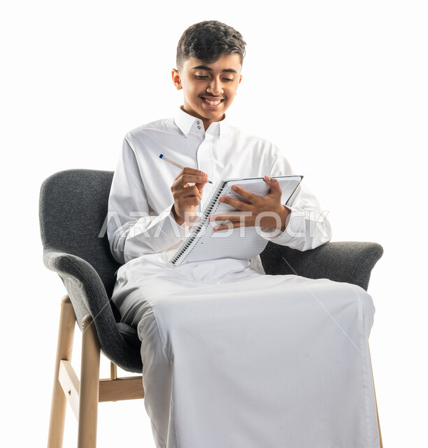 بورتريه لولد عربي سعودي خليجي، يجلس على كرسي، تأدية الواجبات المدرسية، مراجعة الدروس، الإستعداد للعام الدراسي الجديد، التعليم الدراسي في السعودية ، العودة إلى المدارس، المذاكرة للإختبارات المدرسية، خلفية بيضاء