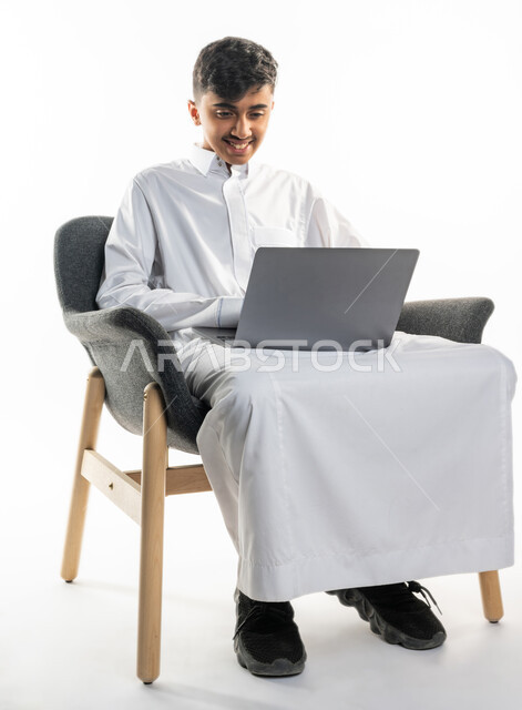 بورتريه لولد عربي سعودي خليجي ، يجلس على كرسي ،   إستخدام جهاز الحاسوب المحمول ، التعليم الإلكتروني ، التعليم عن بعد ، تصفح الإنترنت ، محادثات ودردشة ، خلفية بيضاء