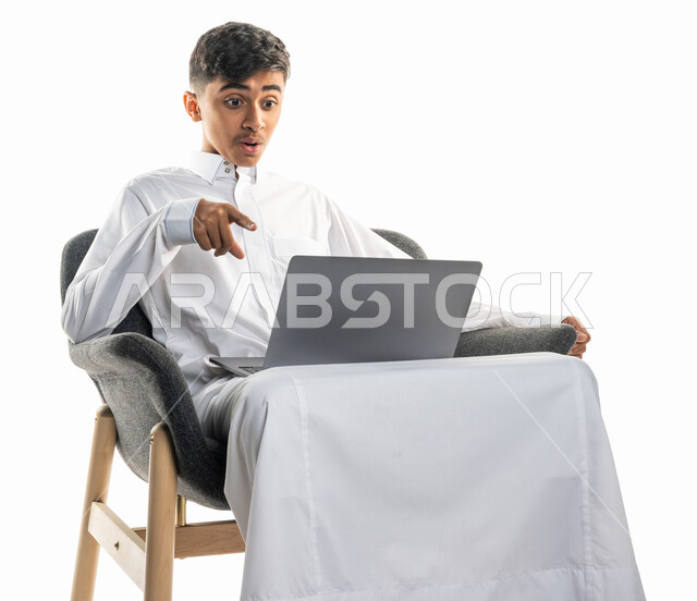 بورتريه لولد عربي سعودي خليجي، يجلس على كرسي،   إستخدام جهاز الحاسوب المحمول، إجراء مكالمة فيديو، تعابير تدل على الدهشة والإستغراب، بث مباشر، التواصل مع الأصدقاء، تصفح الإنترنت، محادثات ودردشة، التعليم الإلكتروني، خلفية بيضاء