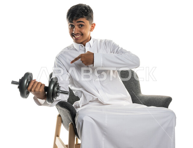 بورتريه لولد عربي خليجي سعودي يجلس على الكرسي، ممارسة التمارين الرياضية مع الدمبل، نشاط بدني للمحافظة على الصحة واللياقة الجسدية، كمال الأجسام، بناء عضل، تمارين رفع الأثقال (دمبلز)، رفع الأوزان الحديدية الثقيلة، خلفية بيضاء