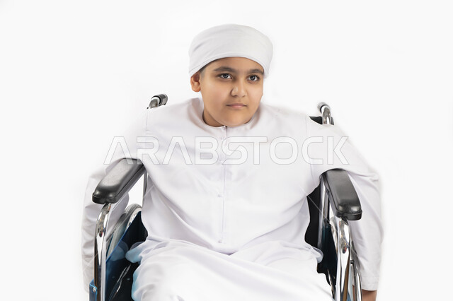 بورتريه لطفل عربي إماراتي خليجي يرتدي الزي التقليدي من ذوي الهمم يجلس على كرسي متحرك ويرتدي الزي التقليدي بإيماءات وجه مبتسمة  , التمكين الاجتماعي, اهتمام ودعم المجتمع الإماراتي لذوي الاحتياجات الخاصه, تقديم الحب و الرعاية و الاهتمام , خلفية بيضاء 