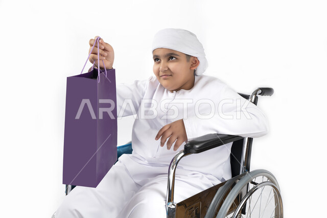 بورتريه لطفل عربي إماراتي خليجي يرتدي الزي التقليدي من ذوي الهمم يجلس على كرسي متحرك و يمسك بيده علبة هدية   , التمكين الاجتماعي, اهتمام ودعم المجتمع الإماراتي لذوي الاحتياجات الخاصه, تقديم الحب و الرعاية و الاهتمام , خلفية بيضاء 