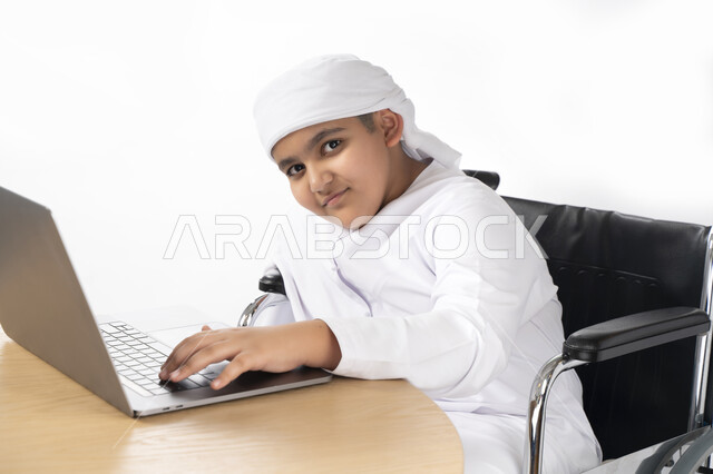 بورتريه لطفل عربي إماراتي خليجي يرتدي الزي التقليدي من ذوي الهمم يجلس على كرسي متحرك يؤدي فروضه المدرسية ,مفهوم التعليم عبر الإنترنت ,  التمكين الاجتماعي, اهتمام ودعم المجتمع الإماراتي لذوي الاحتياجات الخاصه, التعليم المنزلي , تعليم عن بعد , خلفية بيضاء 