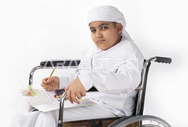 بورتريه لطفل عربي إماراتي خليجي يرتدي الزي التقليدي من ذوي الهمم يجلس على كرسي متحرك يؤدي فروضه المدرسية  , التمكين الاجتماعي, اهتمام ودعم المجتمع الإماراتي لذوي الاحتياجات الخاصه, التعليم المنزلي , تعليم عن بعد , خلفية بيضاء 