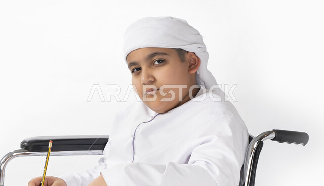 بورتريه لطفل عربي إماراتي خليجي يرتدي الزي التقليدي من ذوي الهمم يجلس على كرسي متحرك يؤدي فروضه المدرسية  , التمكين الاجتماعي, اهتمام ودعم المجتمع الإماراتي لذوي الاحتياجات الخاصه, التعليم المنزلي , تعليم عن بعد , خلفية بيضاء 