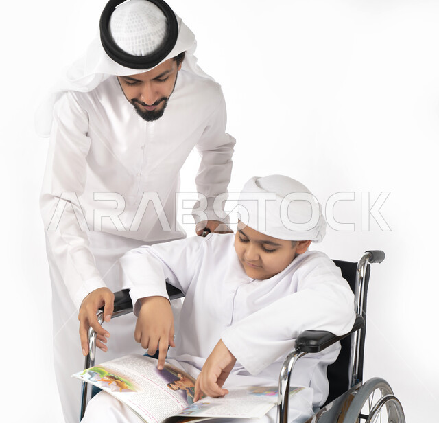 بورتريه لطفل عربي إماراتي خليجي من ذوي الهمم يجلس على كرسي متحرك ويرتدي الزي التقليدي كندورة وعمامه يقرأ مع والده كتاب قصص  ، التمكين الاجتماعي  ، اهتمام ودعم المجتمع الإماراتي لذوي  الاحتياجات الخاصه، شعور ذوي الهمم بالراحه والطمأنينه في بيئتهم , خلفية ب