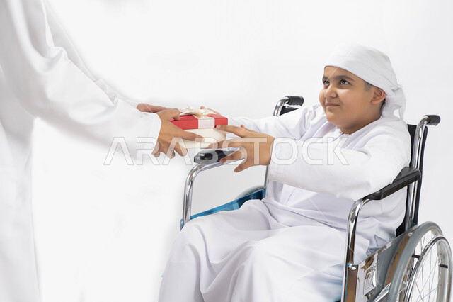 بورتريه لطفل عربي إماراتي خليجي يرتدي الزي التقليدي من ذوي الهمم يجلس على كرسي متحرك و يمسك بيده علبة هدية   , التمكين الاجتماعي, اهتمام ودعم المجتمع الإماراتي لذوي الاحتياجات الخاصه, تقديم الحب و الرعاية و الاهتمام , خلفية بيضاء 