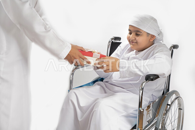 بورتريه لطفل عربي إماراتي خليجي يرتدي الزي التقليدي من ذوي الهمم يجلس على كرسي متحرك و يمسك بيده علبة هدية   , التمكين الاجتماعي, اهتمام ودعم المجتمع الإماراتي لذوي الاحتياجات الخاصه, تقديم الحب و الرعاية و الاهتمام , خلفية بيضاء 
