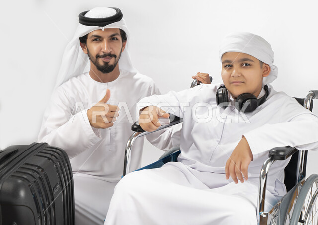 بورتريه لطفل عربي إماراتي خليجي من ذوي الهمم يجلس على كرسي متحرك ويرتدي الزي التقليدي كندورة وعمامه مستعد لسفر مع والده  ، التمكين الاجتماعي  ، اهتمام ودعم المجتمع الإماراتي لذوي  الاحتياجات الخاصه، شعور ذوي الهمم بالراحه والطمأنينه في بيئتهم , خلفية بيضا