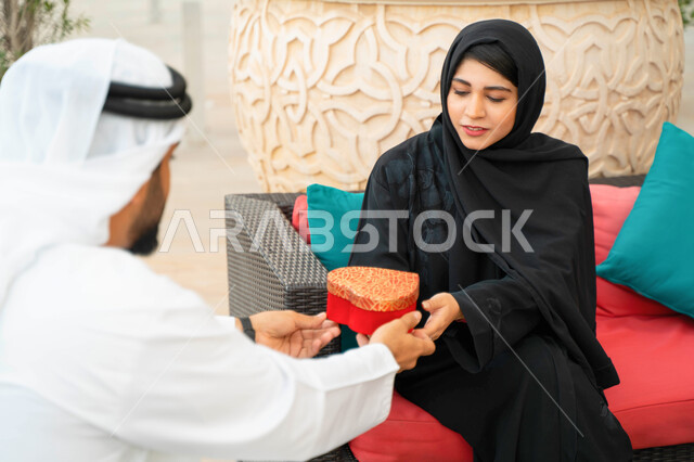 A Saudi man and woman celebrate Valentine's Day in a luxurious resort. The concept of intimacy and love between spouses, gestures indicating happiness and pleasure, sharing and giving gifts on holidays and family occasions, an Arab Gulf Emirati lady prese