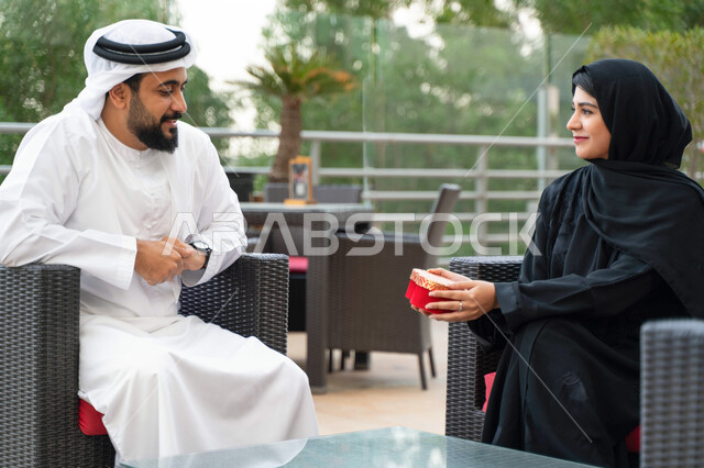 مفهوم الألفة والمحبة بين الزوجين، ايماءات تدل على السعادة والسرور, مشاركة وتقديم الهدايا في الأعياد والمناسبات العائلية, سيدة عربية خليجية إماراتية تقدم لزوجها هدية بمناسبة ذكرى يوم الزواج, رجل وإمرأة سعوديان يحتفلان بعيد الحب في إحدى المنتجعات الفاخرة