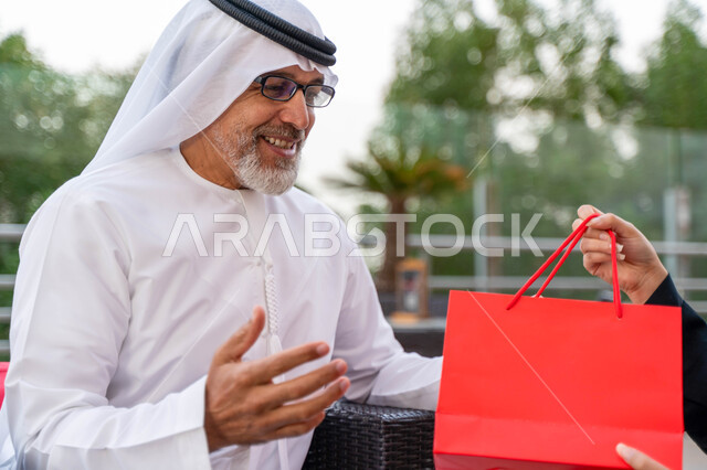 مفهوم الاهتمام والتقدير وبر الوالدين، تقديم الهدايا للآباء بمناسبة عيد الأب، صورة مقربة لرجل مسن عربي اماراتي يرتدي الكندورة والغترة بايماءات تدل على الفرح والاندهاش، رجل سعودي  يقضي أوقات ممتعه في أحد المزارع في الخارج، أجواء أسرية مليئة بالحب