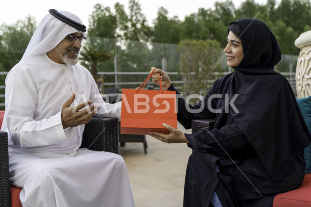 احترام وتقدير وبر الوالدين، مفهوم الترابط الاسري، سيدة عربية اماراتية خليجية تجلس مع والدها في أحد المقاهي، المناسبات العائلية السعيدة، شابة سعودية محجبة  تقوم بتقديم هدية رمزية لوالدها بمناسبة يوم الاب، ايماءات تدل على السعادة والسرور والحب