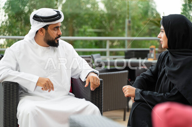  الترابط الفكري و التفاهم بين الزوجين، تبادل الدردشات و الأحاديث في الخارج، التنزه في الهواء الطلق، رجل عربي اماراتي يجلس مع زوجته بأحد المقاهي الفاخرة، سيدة سعودية محجبة ترتدي العباءة الخليجية تقضي أوقات مميزة مع زوجها.