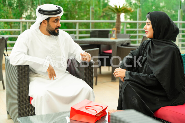 تقديم الهدايا بالأعياد والمناسبات، تبادل الدردشات والأحاديث والتنزه في الهواء الطلق، مفهوم الترابط الفكري والتفاهم بين الزوجين، رجل عربي اماراتي يجلس مع زوجته بأحد المقاهي الفاخرة، سيدة سعودية محجبة ترتدي العباءة الخليجية تقضي أوقات مميزة مع زوجها.