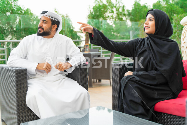 الاشارة الى شيء معين، زوجان عربيان اماراتيان يقومان بالتنزه في الهواء الطلق بأحد المنتجعات الفاخرة، قضاء أوقات مميزة بين الزوجين و تبادل الاحاديث والدردشات في الخارج، سيدة سعودية محجبة ترتدي العباءة الخليجية و تشير الى شيء ما