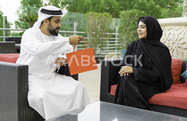 مفهوم الألفة والمحبة بين الزوجين، ايماءات تدل على السعادة والسرور, مشاركة وتقديم الهدايا في الأعياد والمناسبات العائلية, رجل عربي خليجي إماراتي يقدم لزوجته هدية بمناسبة ذكرى يوم الزواج, رجل وإمرأة سعوديان يحتفلان بعيد الحب في إحدى المنتجعات الفاخرة