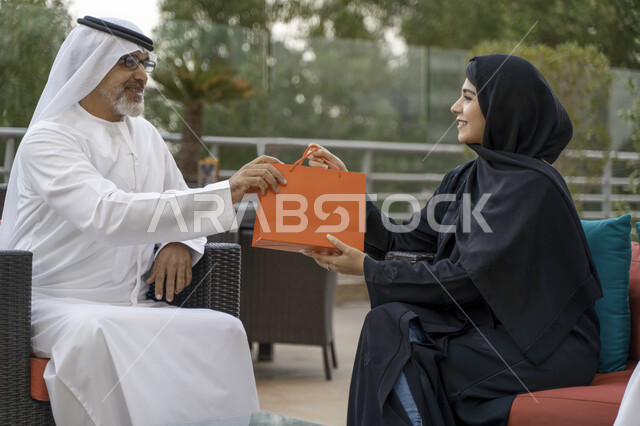 تقدير واحترام وبر الوالدين، الإستمتاع بأجواء عائلية سعيدة في الخارج، صورة مقربة لسيدة سعودية محجبة تقوم بتقديم هدية لوالدها بمناسبة عيد الأب، عائلة عربية خليجية اماراتيه تقضي أوقات ممتعه في أحد المزارع،  مفهوم صلة الرحم.